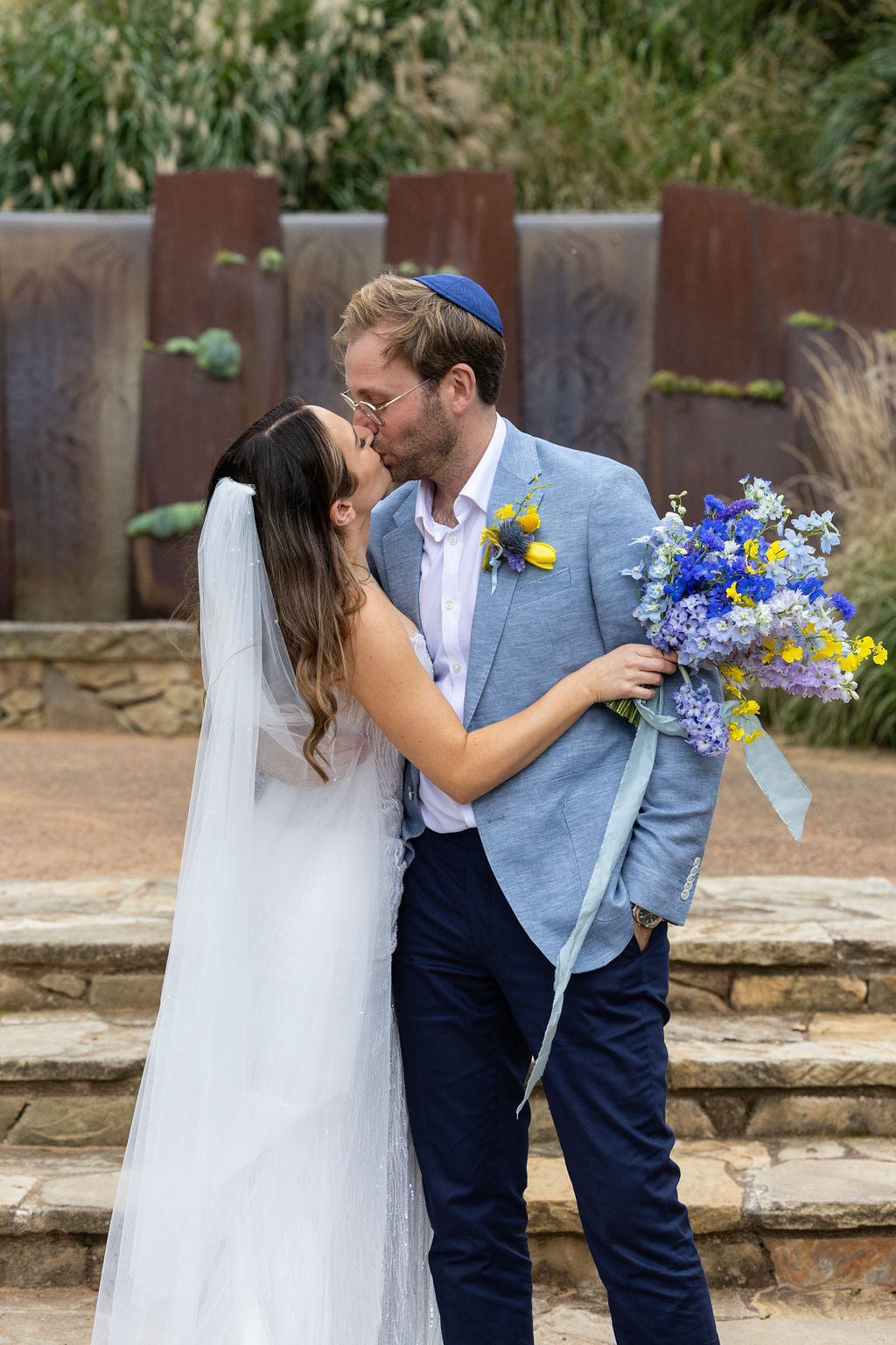 Sophie and Alex kissing outside The Stables at Bendooley Estate, with her blue and yellow bouquet