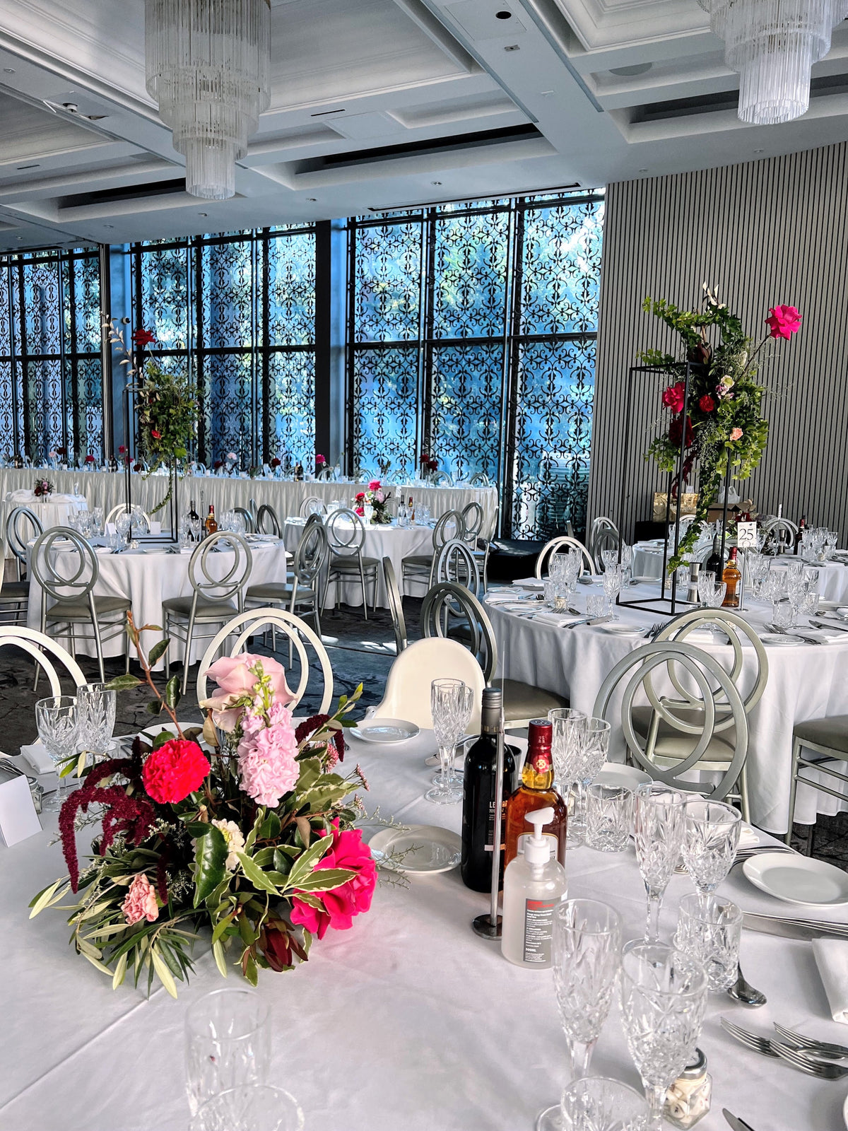 The Curzon Hall reception room set with round white tables, crystal chandeliers and a pink and red floral centrepiece