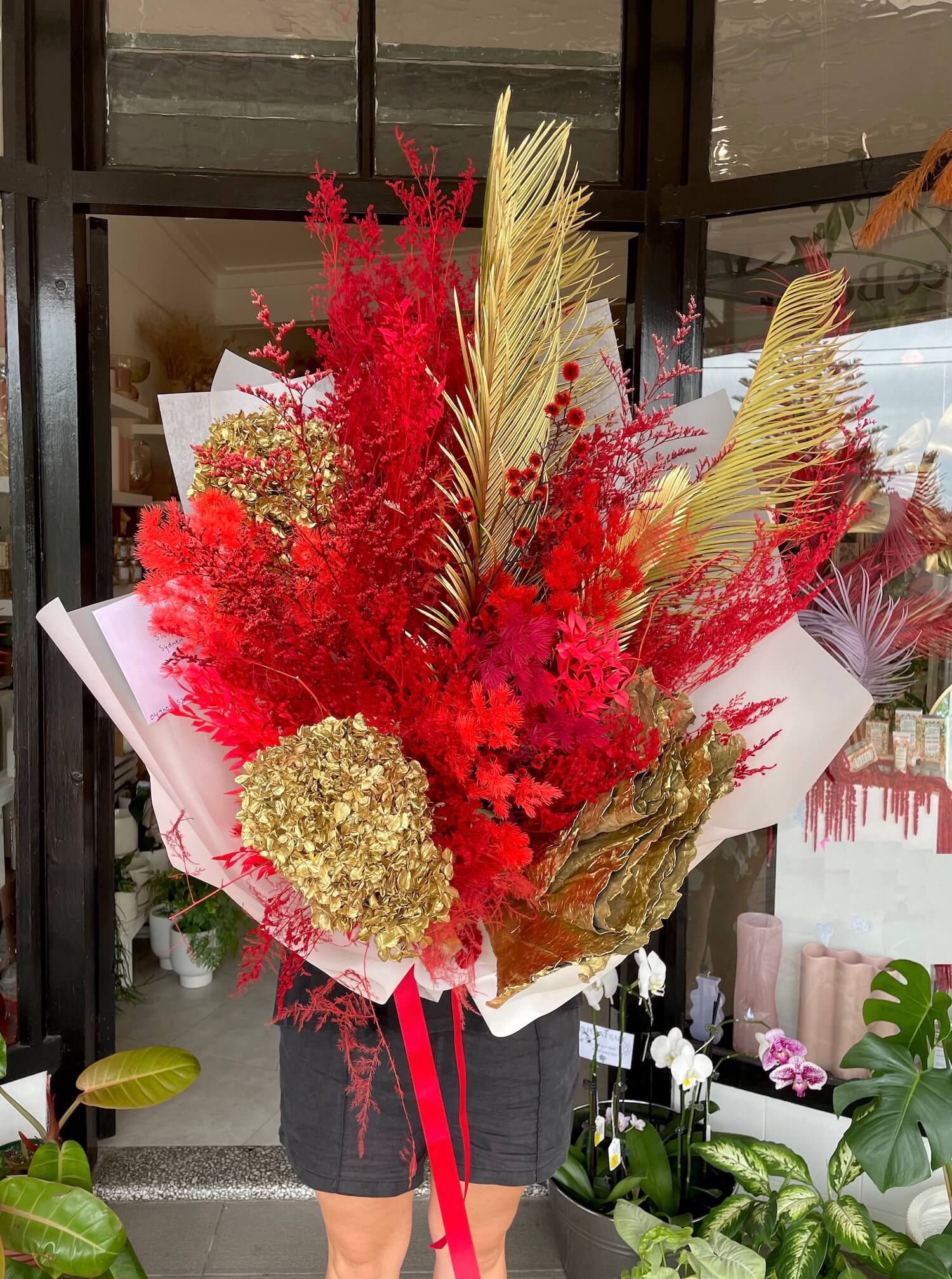 Bouquet of red and gold everlasting dried flowers for lunar chinese new year, with a person partially visible in the background.