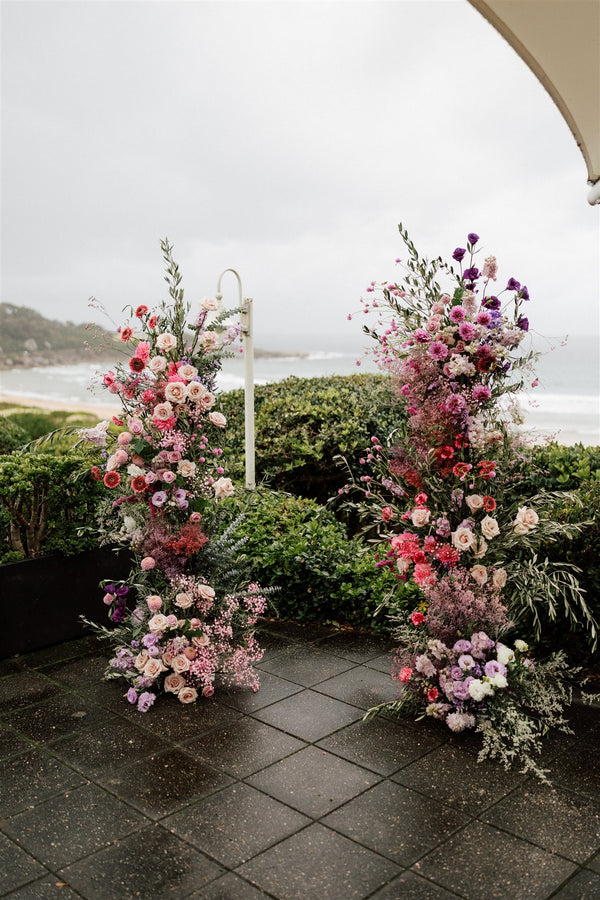 Floral arches with pink and purple lilac wedding flowers designed freestanding on the floor by a beach in sydney