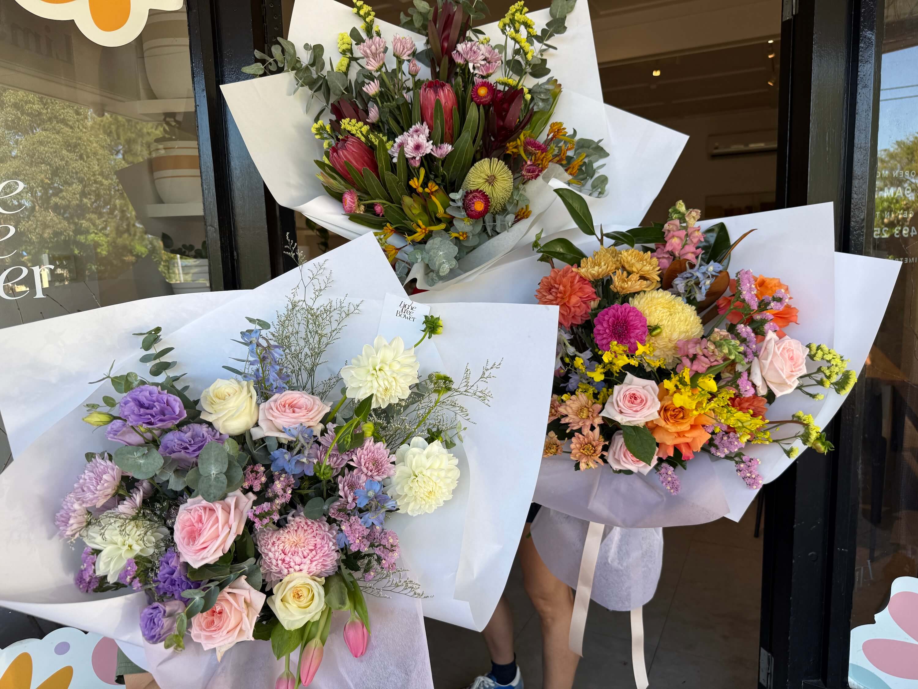 Three modern flower bouquets on white paper in front of a store entrance for mothers day sydney.
