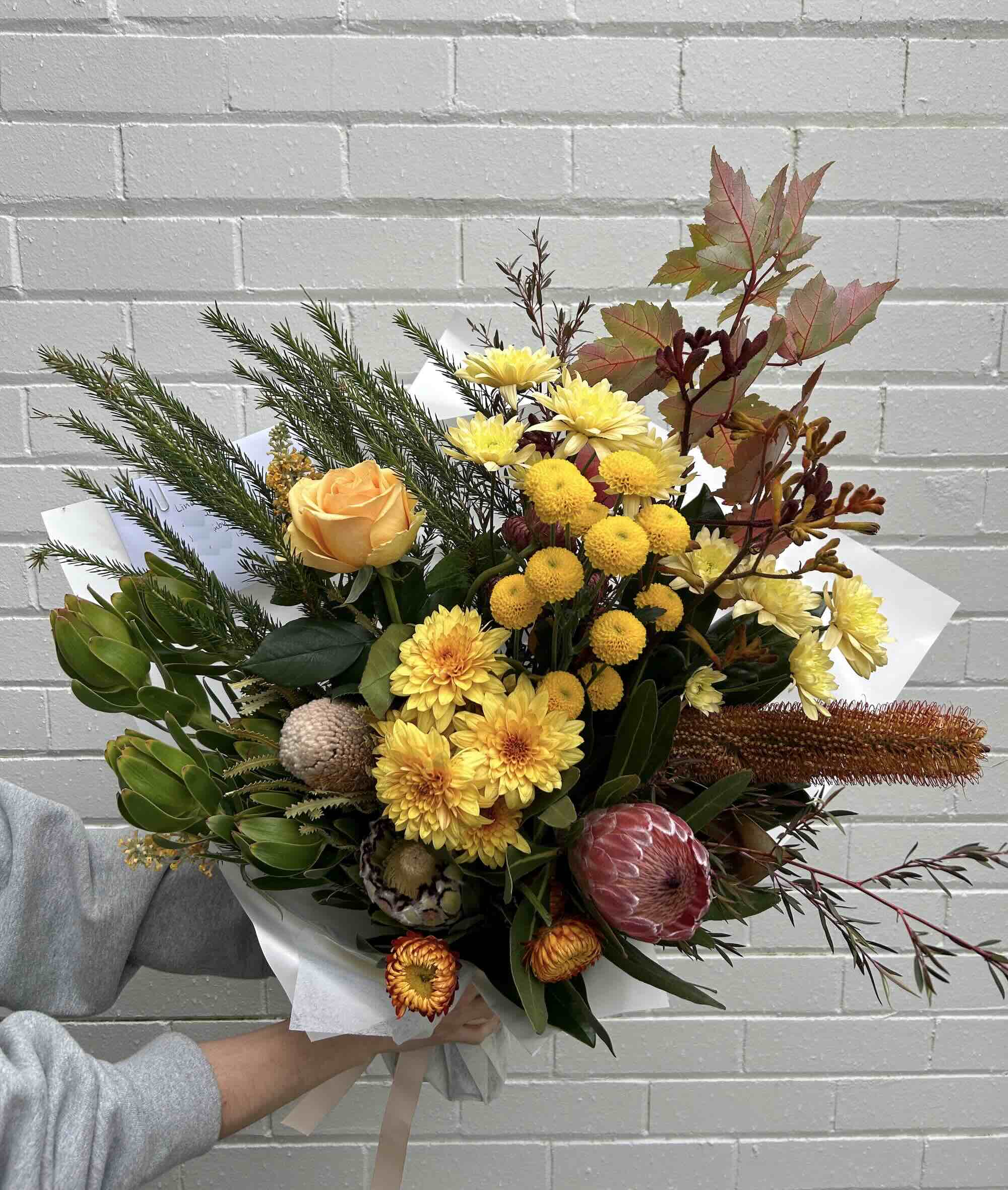 A bouquet of native flowers in various colours including yellow, red, and green, held against a white background.