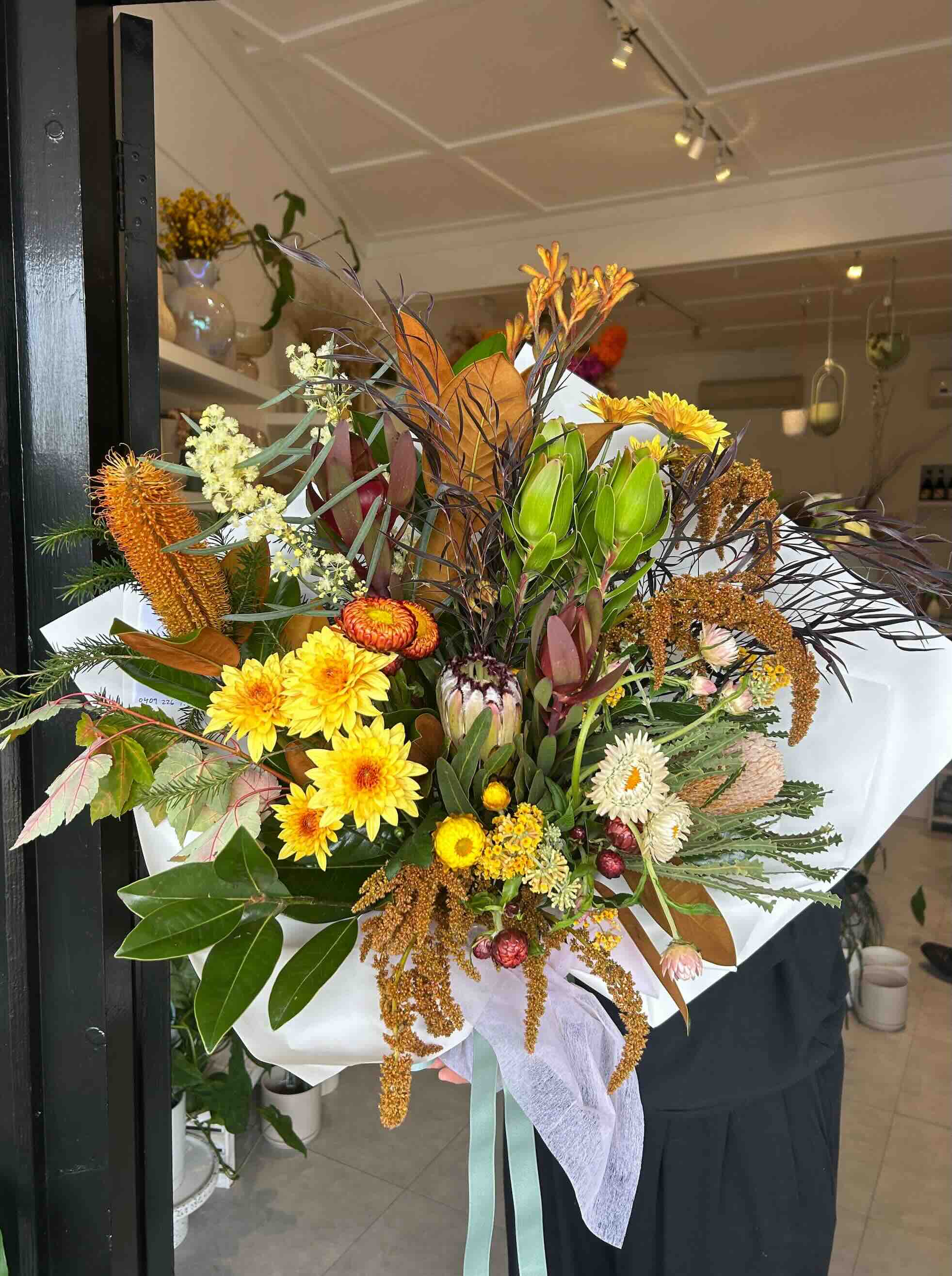 A bouquet of native Australian flowers in a range of colors including yellow, green, and brown, tied with ribbons and ready for gift-giving.
