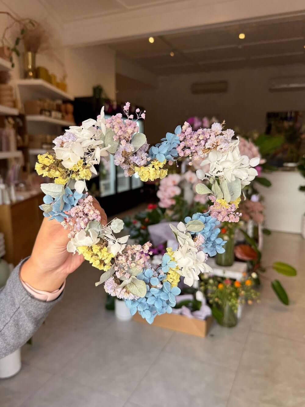 Hand holding a colourful floral wreath inside flower shop for a pet funeral tribute