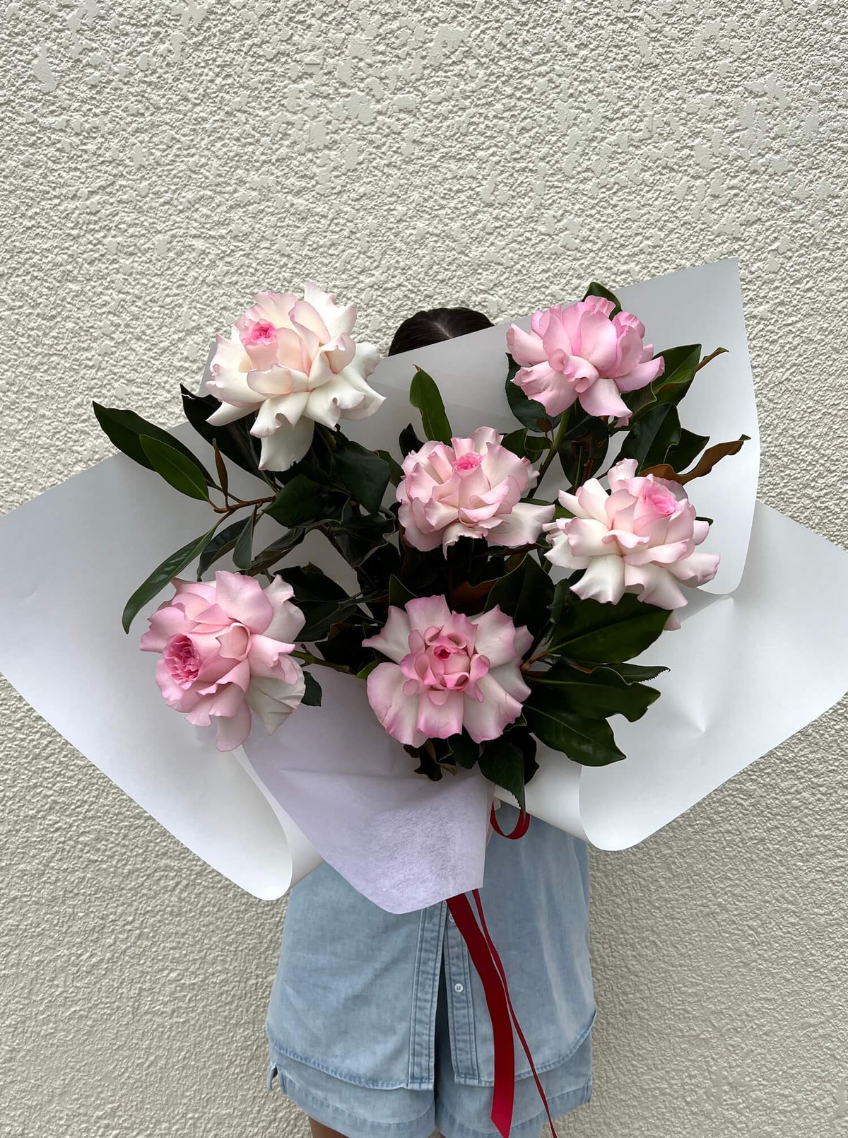 Bouquet of half dozen light pink premium roses for valentines day gifting wrapped in white paper against a creamy white wall background