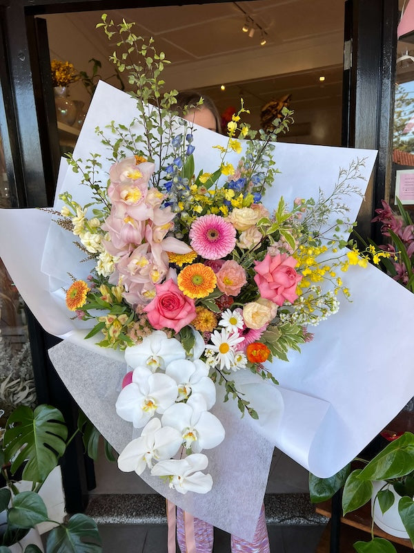 Bouquet of colourful flowers with white and pink orchids, seasonal local flowers, roses, gerberas, poppies, daisies, wrapped with white paper