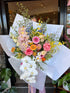 Bouquet of colourful flowers with white and pink orchids, seasonal local flowers, roses, gerberas, poppies, daisies, wrapped with white paper