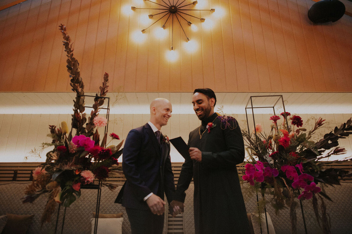 Two grooms at their ceremony in The Burbs at Ovolo Woolloomooloo with bright floral clusters on geometric stands