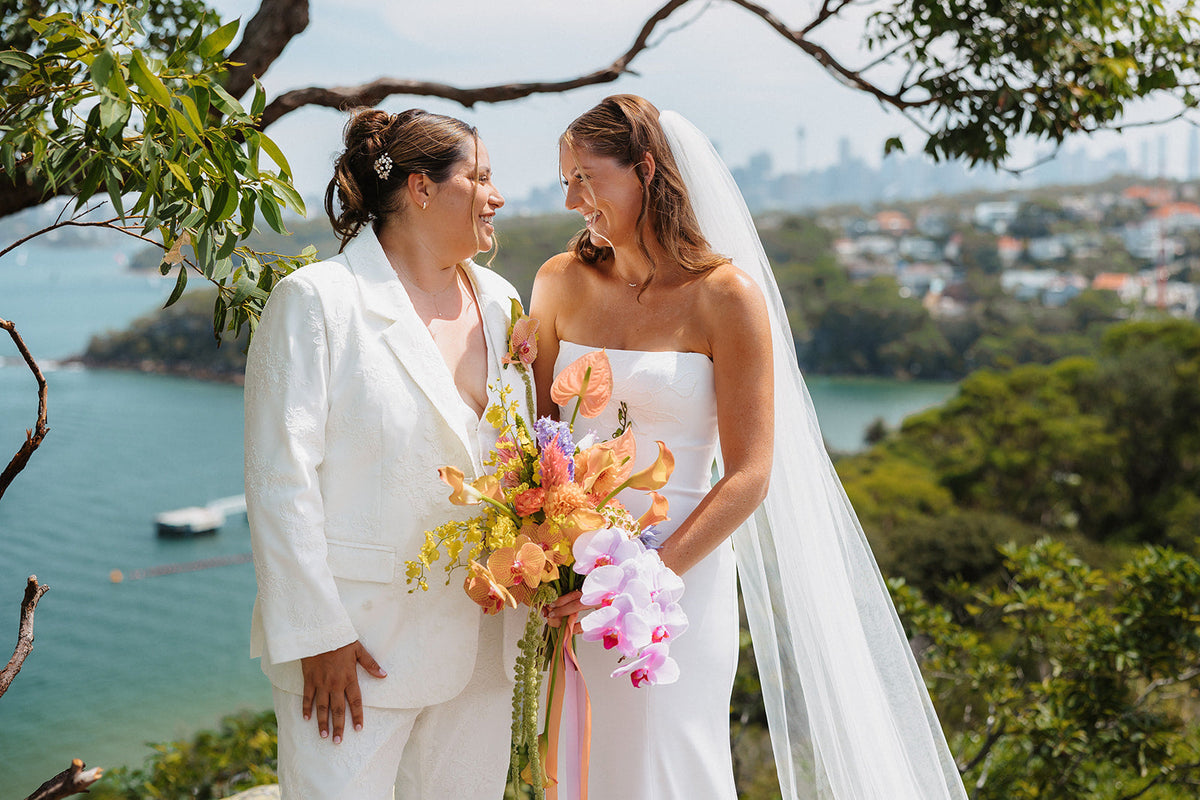 Mollie and Izzy on the lawn at Sergeants Mess with the harbour behind and a bright orchid bouquet