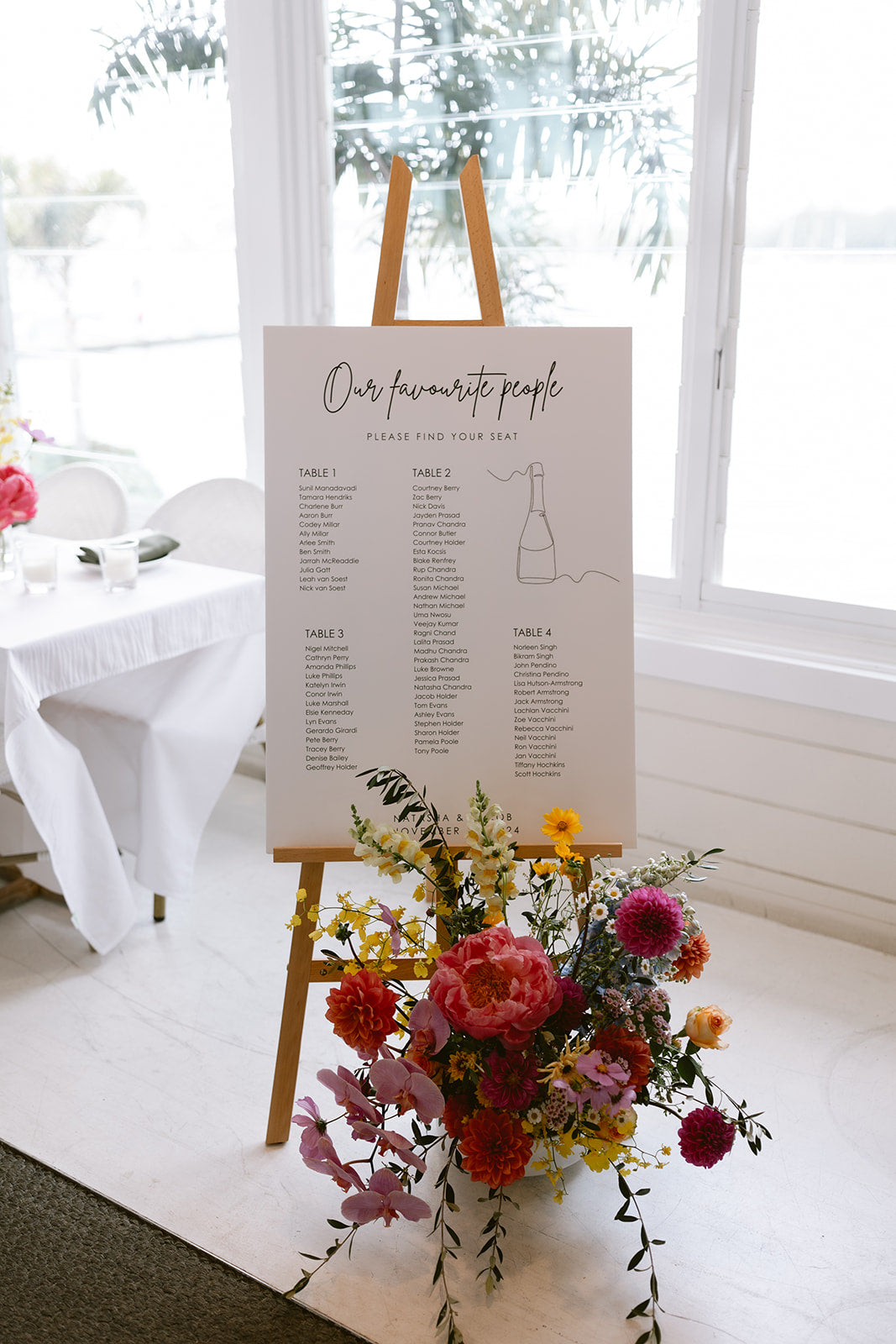 Wedding seating chart on a timber easel with a coral and red floor arrangement at The Boathouse Rose Bay, by Lime Tree Bower Florist