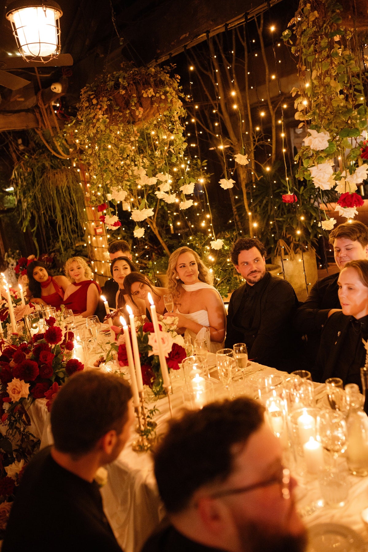 Couple and bridal party at the long table under hanging white roses at The Grounds of Alexandria
