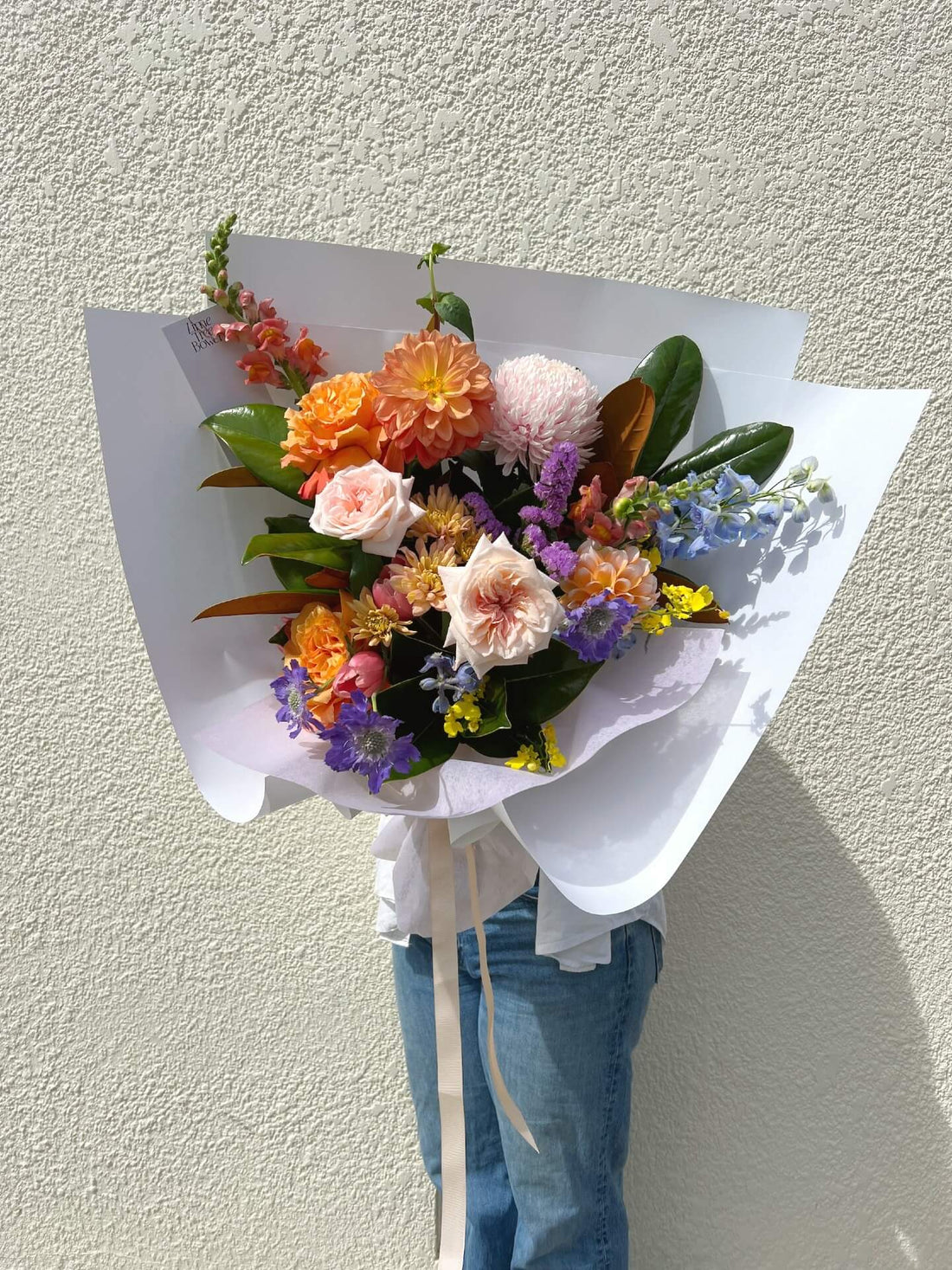 wrapped bouquet for mothers day gift with orange dahlias seasonal local garden roses delphinium magnolia and orchids snapdragon chrysanthemum