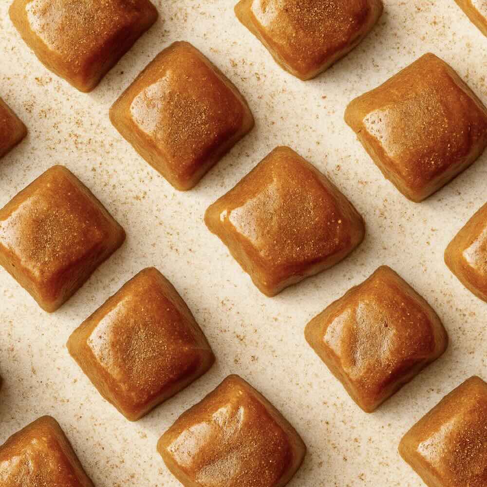 Pattern of square-shaped chai caramel brown candies on a light beige background
