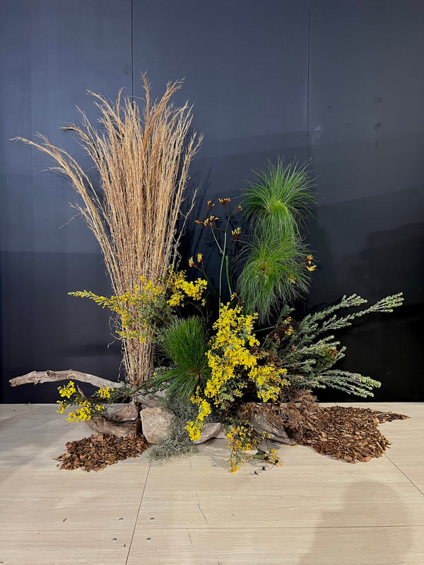 Decorative floral installation arrangement of grasses, foliage, native flowers and dried flowers against a dark backdrop on the floor for a sydney corporate event