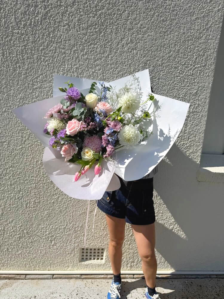 Person holding a bouquet of mothers day flowers in pastel colours against a gray wall