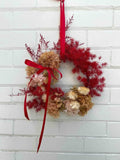 Decorative wreath with red and gold elements on a white brick wall