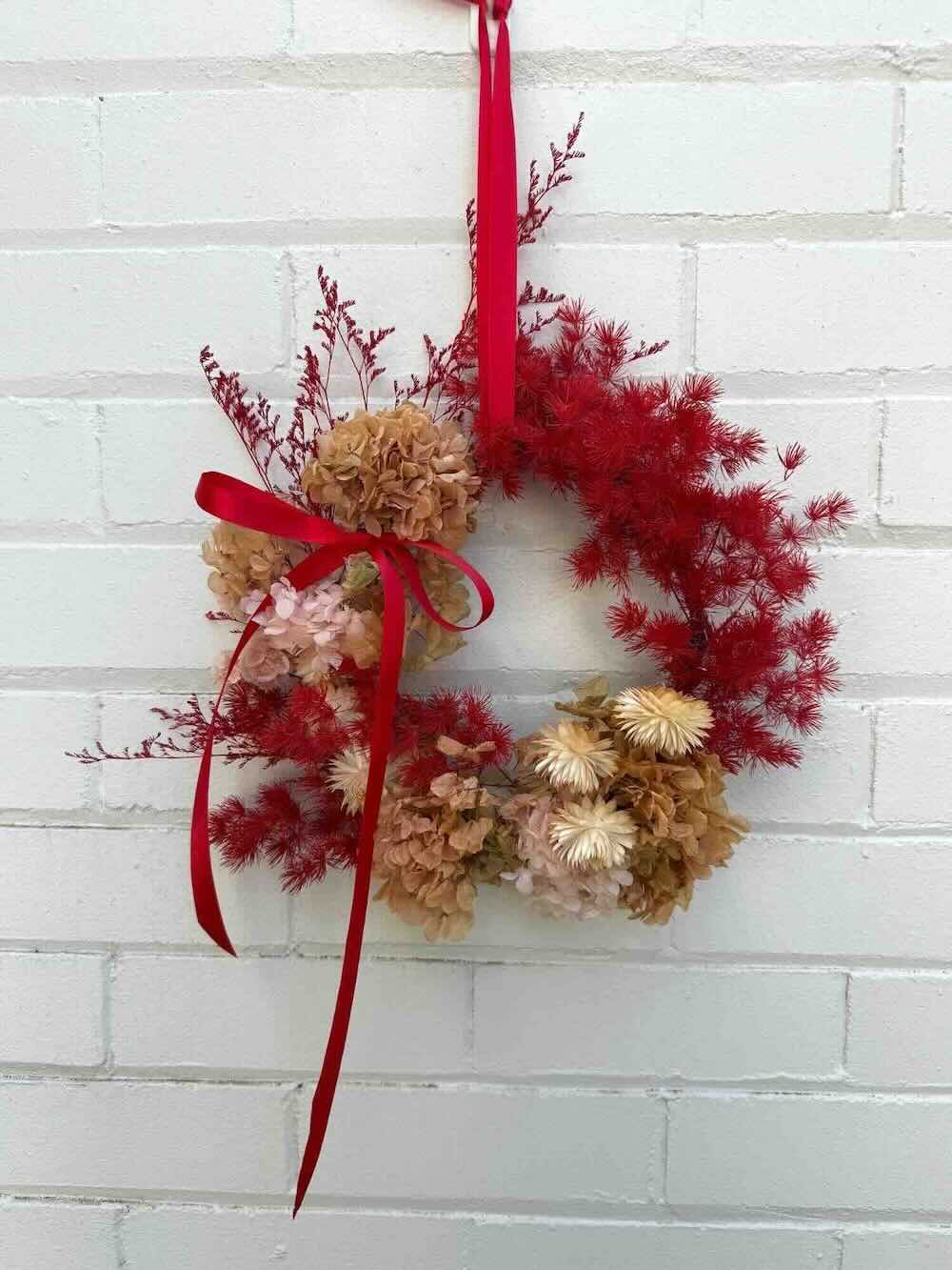 Decorative wreath with red and gold elements on a white brick wall