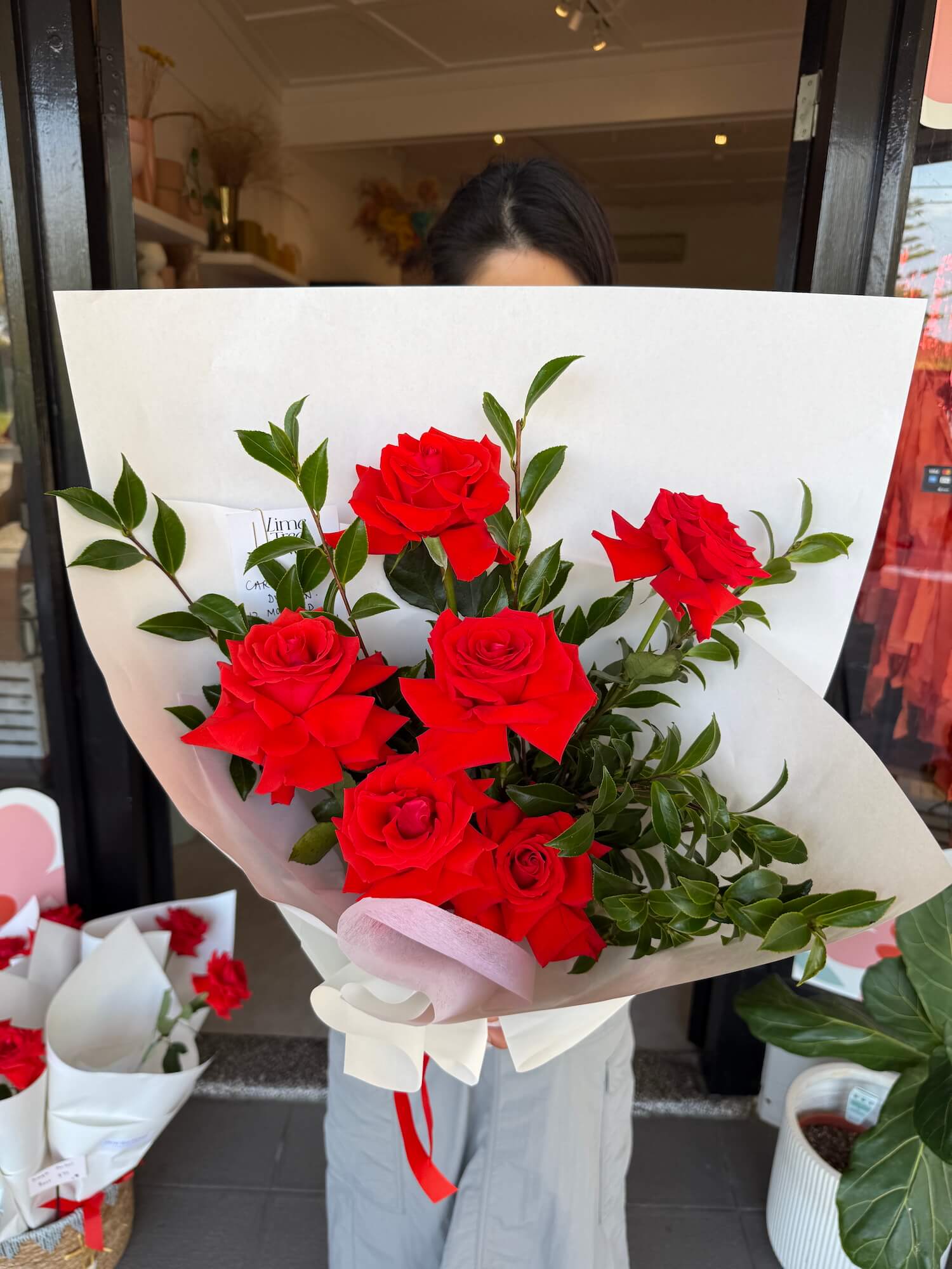 Bouquet of 6 red roses for valentines day gift held by a person outside of sydney flower shop